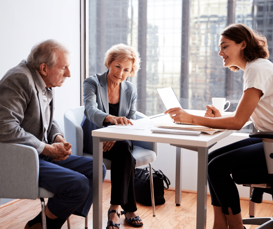 A couple in their 60s sit across the table from a financial adviser.   They are all smiling.