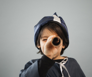 A small child dressed as a wizard looks through a toy telescope
