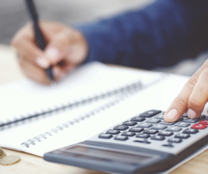 Someone types numbers into a calculator while writing down figures in a notebook