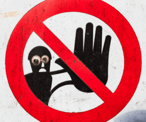 A brick wall painting of a STOP sign (red circle with line through it).  There is also a drawing of a man inside the stop sign with his hand held up to say stop.