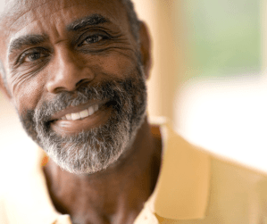 A black man with a beard smiles at the camera.  He is wearing a yellow polo shirt.