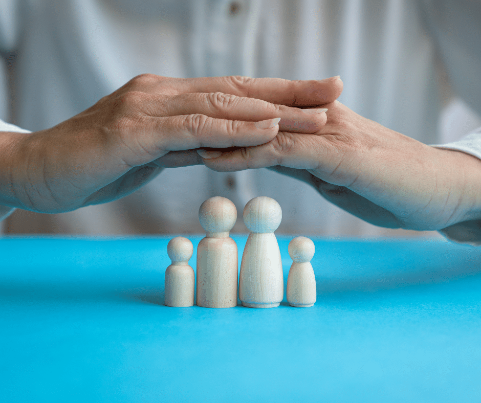 A model of a family sits on a table, with a pair of protective hands being held over it.