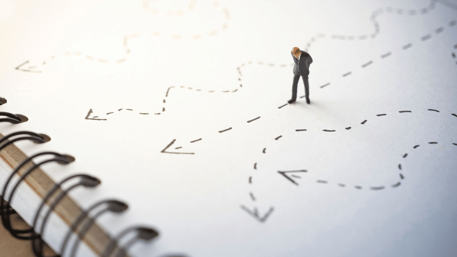 Navigating Man figurine on a piece of paper in a notebook standing on a dotted line with an arrow with other dotted lines with arrows around him
